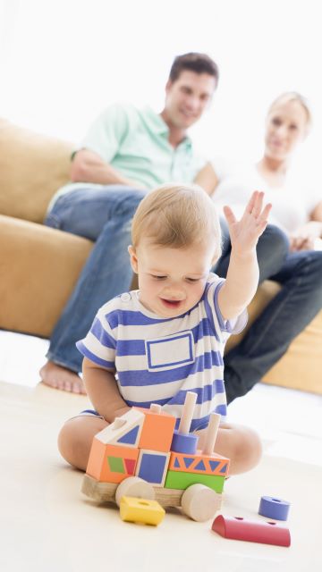 photo of a young couple in their living room watching their toddler child play in peace