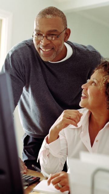 photo of an old couple having a joyful conversation over a desk facing a computer screen