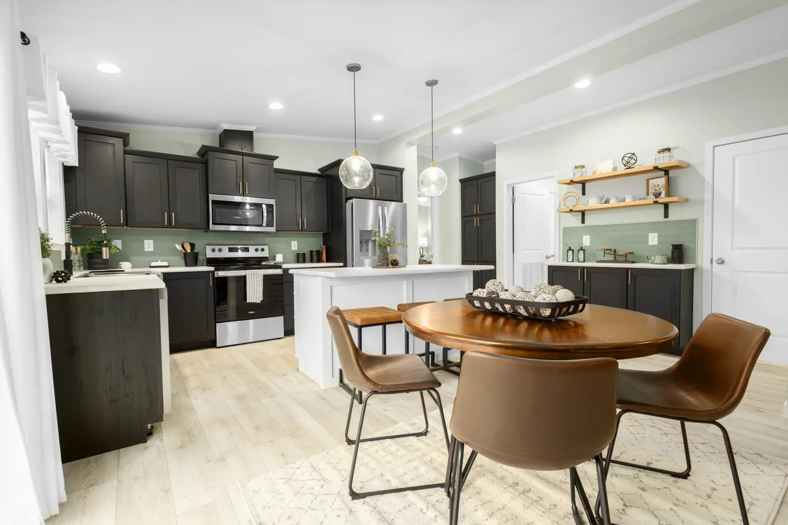 Cavco – Dorchester Westlake Outlook sleek and modern home with vaulted ceiling, modern green cabinetry with gold accents, top of the line appliances, pendant lighting and walnut-colored plank flooring.