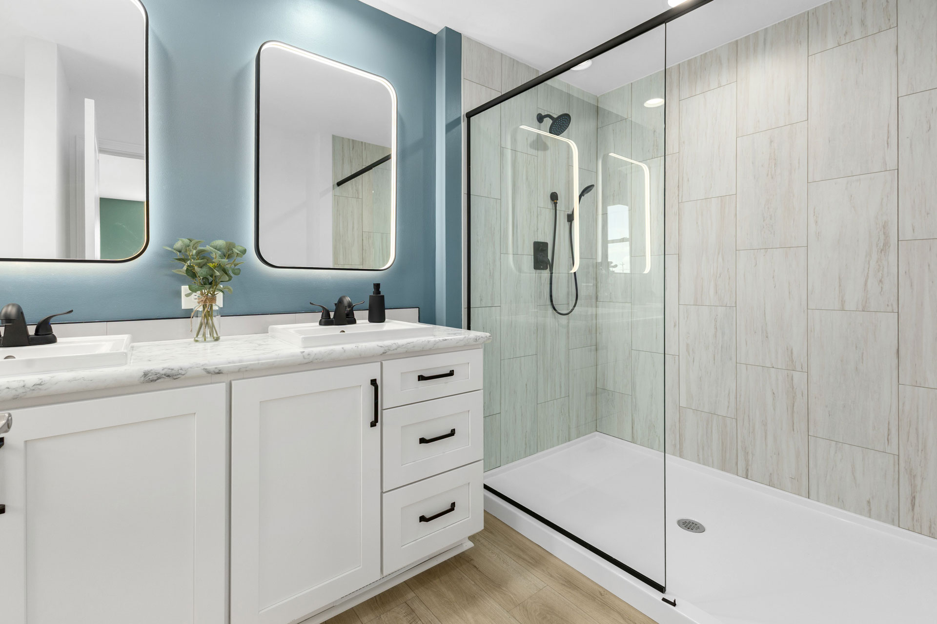 A modular home’s primary bath that offers a side-by-side his-and-hers sink with vanity, spacious walk-in shower, plenty of storage and soft LED lighting.