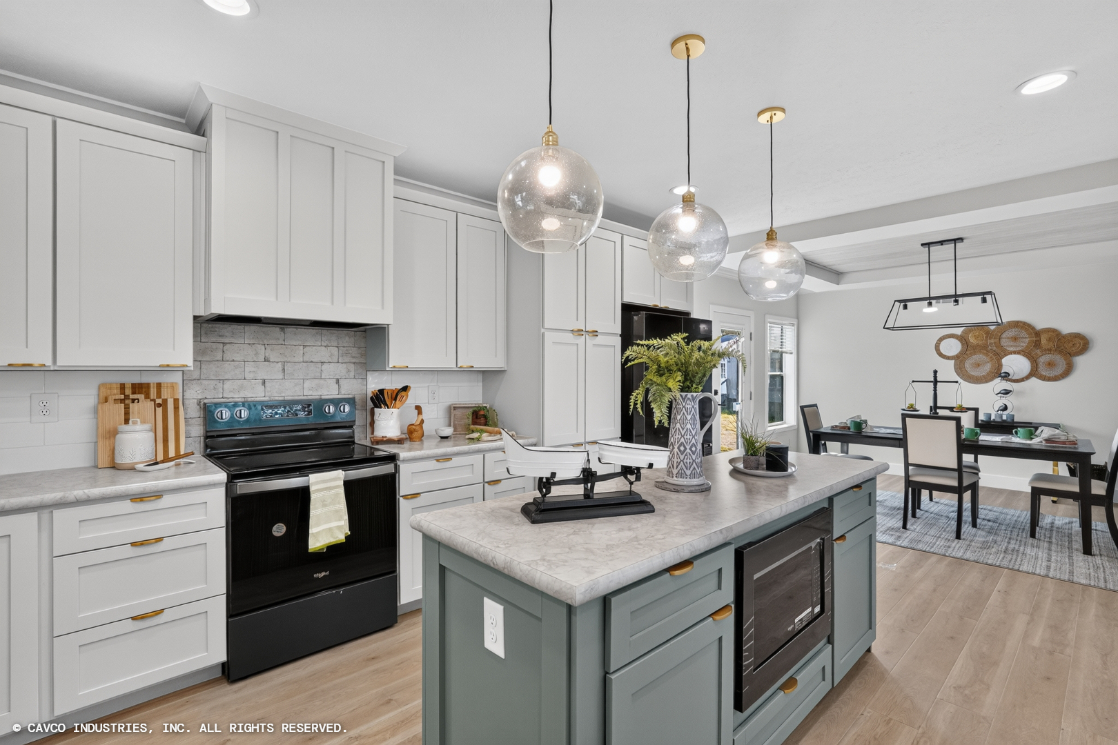 Cavco – Dorchester Westlake Outlook sleek and modern home with vaulted ceiling, modern green cabinetry with gold accents, top of the line appliances, pendant lighting and walnut-colored plank flooring.