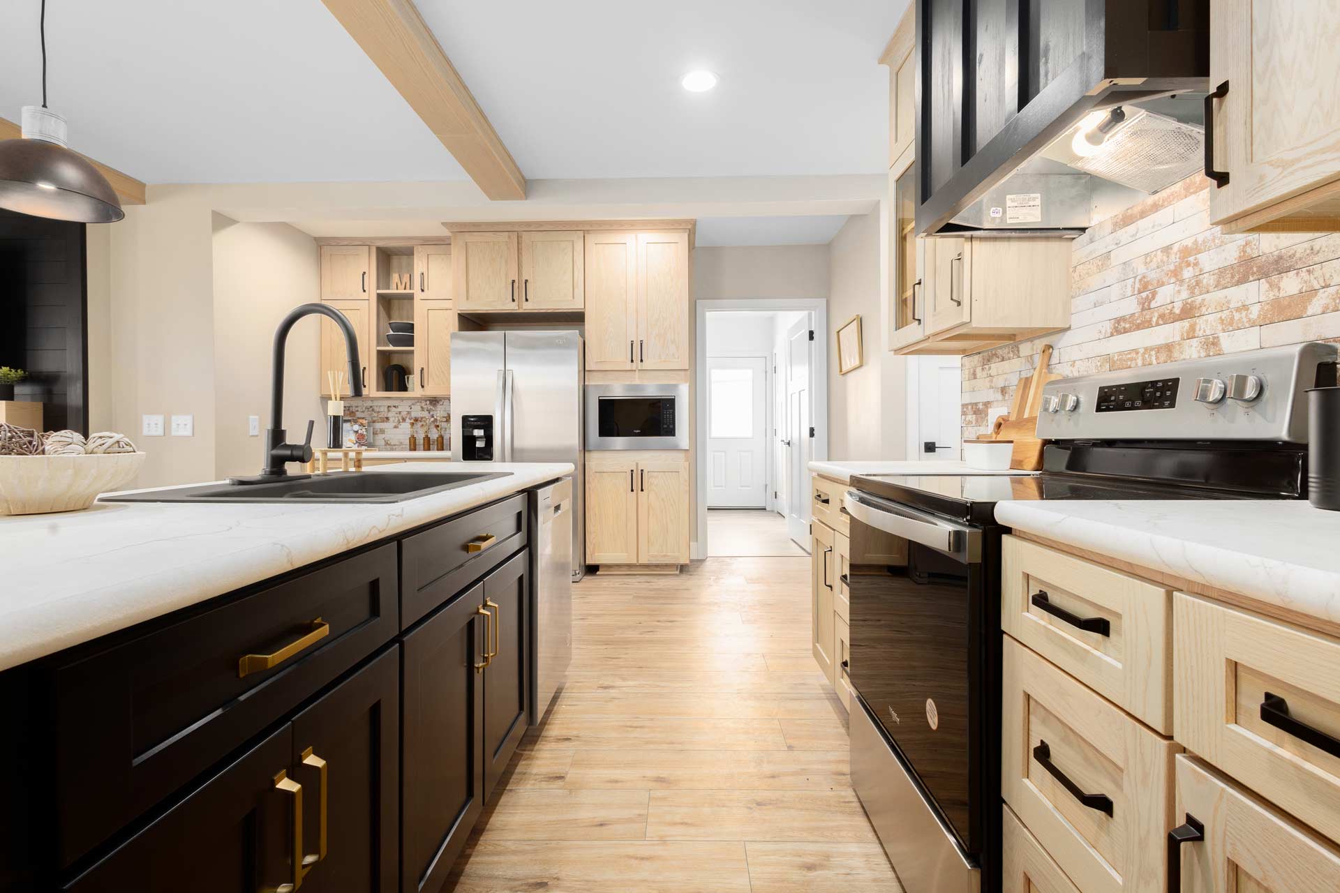 Highest KCMA and ANSI standards Cavco Manorwood luxury kitchen modular manufactured home with ample storage, solid cabinets, gorgeous plank wood flooring, navy kitchen island with gold hardware trim, black sink, energy-efficient appliances.